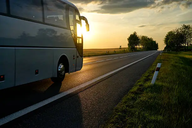 Photo of White Bus driving along the asphalt road at sunset.