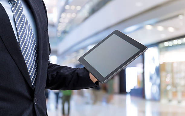 istock isolated business man hold the tablet  on shopping mall background 614317892