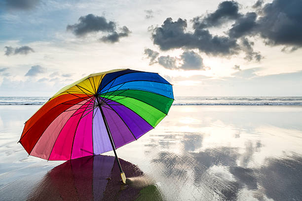 abstract multi colored rainbow umbrella on the beach at sunset - rainbow umbrella descriptive color multi colored imagens e fotografias de stock