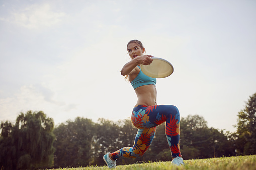 Young athletic girl playing with flying disc in the park. Professional player. Sport concept. Ultimate