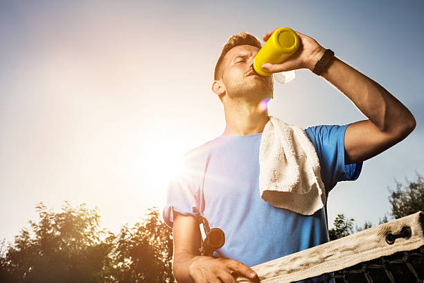 Below view of thirsty male tennis player having refreshment and drinking form water bottle.