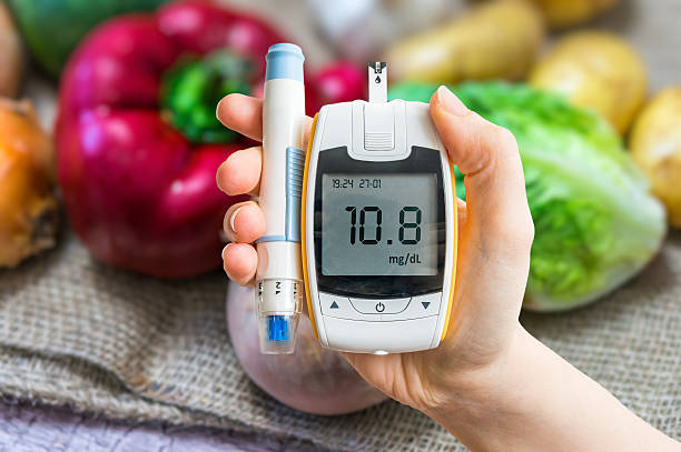 Diabetic diet, diabetes concept. Hand holds glucometer. Vegetables in background. stock photo