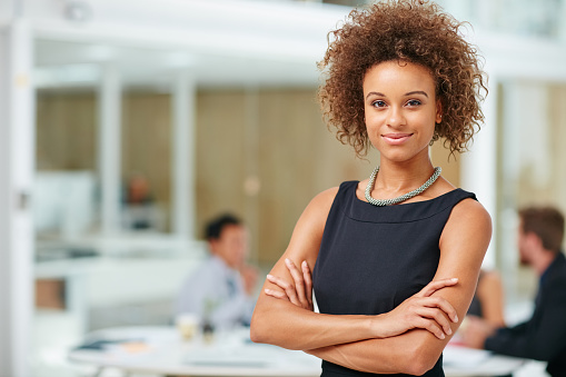 Portrait of a smiling young businesswoman standing with her arms crossed in a modern office