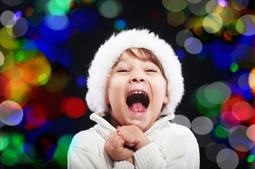 happy little boy screaming from the amazing christmas concept santa hat bokeh light at background