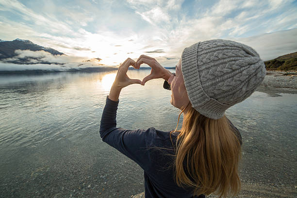 istock Blond girl by the lake makes heart shape finger frame 614342870