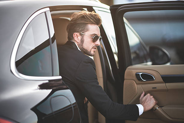 istock Man with sunglasses exiting the black car 614343764