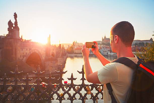 Tourist in Prague Traveler with backpack taking photo by mobile phone. Young tourist near Charles bridge at the sunset. Prague, Czech Republic. - back lit cityscape videos stock pictures, royalty-free photos & images