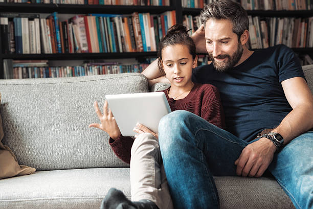 padre felice e figlia al divano guardando tablet digitale - child candid indoors lifestyles foto e immagini stock