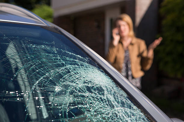 woman phoning for help after car windshield has broken - carro quebrado imagens e fotografias de stock