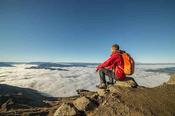 istock Young man hiker sits on mountain peak above the clouds 614348612