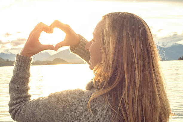 istock Female makes heart shape finger frame on lake mountain landscape 614348762
