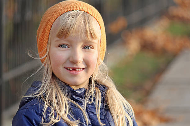 Beautiful blonde girl smiling. Deciduous tooth fell out. Natural light in the autumn park.