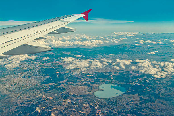 cross-processed aerial photo of mountains and heart shaped lake from airplane window on clear sunny day with part of plane wing visible