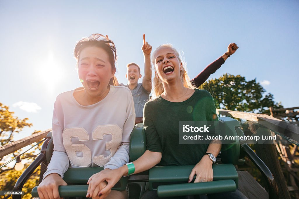 Enthusiastic young friends riding amusement park ride Enthusiastic young friends riding roller coaster ride at amusement park. Young people having fun at amusement park. Rollercoaster Stock Photo