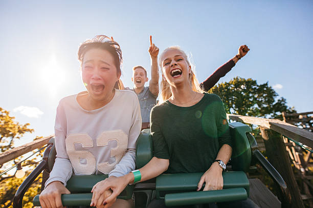 Enthusiastic young friends riding amusement park ride Enthusiastic young friends riding roller coaster ride at amusement park. Young people having fun at amusement park. riding stock pictures, royalty-free photos & images