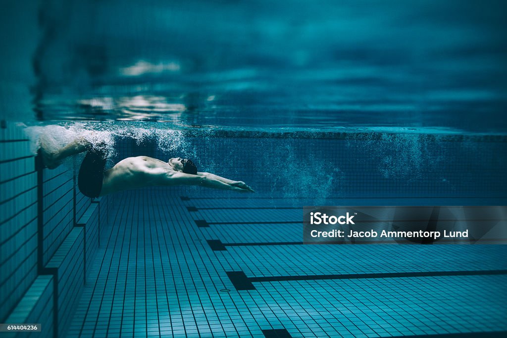 Male swimmer turning over in swimming pool Underwater shot of male swimmer turning over in swimming pool. Pro male swimmer in action inside pool. Swimming Stock Photo