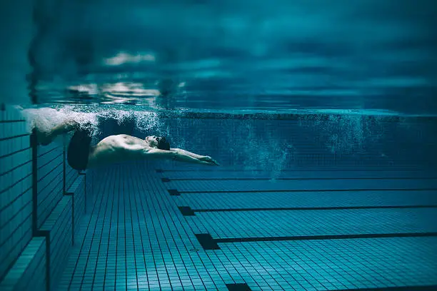Underwater shot of male swimmer turning over in swimming pool. Pro male swimmer in action inside pool.
