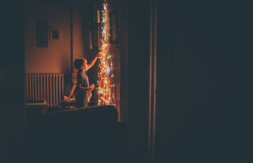 Young boy is getting ready for Christmas. The main focus are Christmas lights. The photo taken from the mirror
