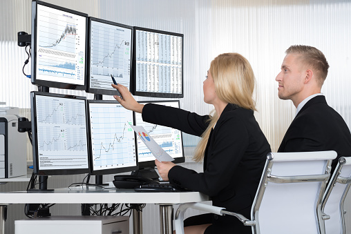 Financial workers analyzing data displayed on computer screens at desk in office