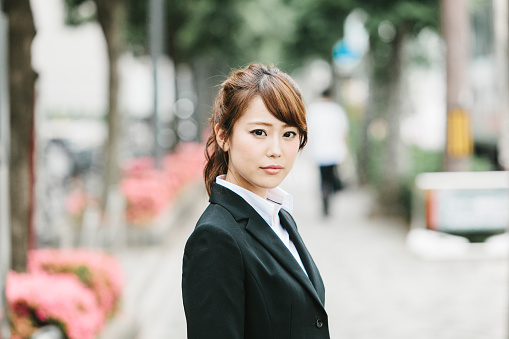 An Asian Businesswoman standing on the streets of Kyoto, Japan. She has a kind look on her face though her work is tough. Wearing formal business wear to keep her professional look, she has to handle many client and entrepreneur situations on daily basis. Yet manages to be kind-hearted and humane towards people while handling their ideas, conceptions and problems day in day out.