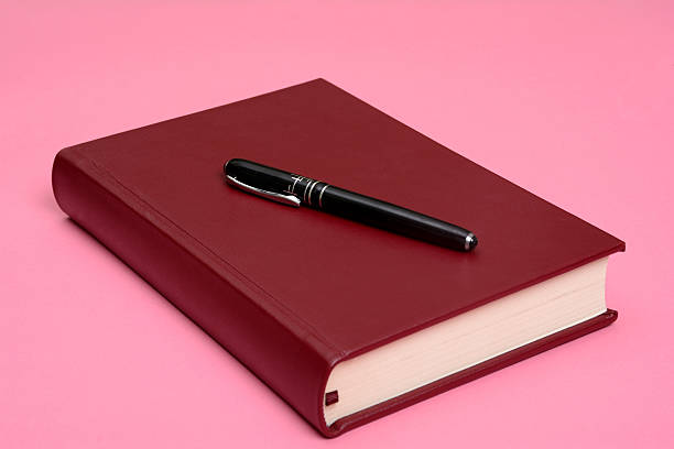 istock Red Book with Pen on Top Isolated on Pink Background 614413572