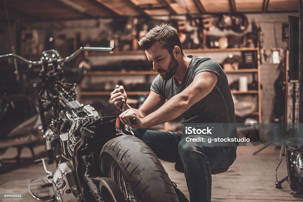 This bike will be perfect. Confident young man repairing motorcycle in repair shop Motorcycle Stock Photo