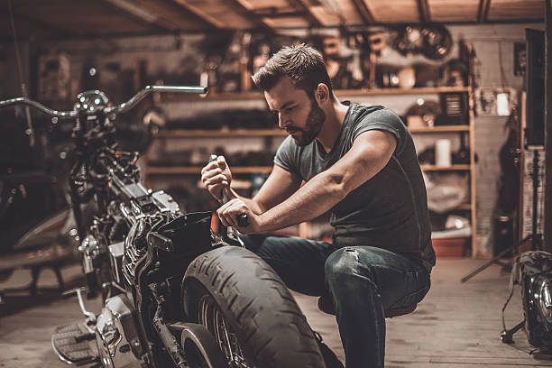 This bike will be perfect. Confident young man repairing motorcycle in repair shop squatting position photos stock pictures, royalty-free photos & images