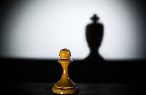 istock chess pawn casting a king piece shadow in dark 614418416