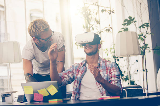 Entrepreneurs testing virtual reality technology with colleague stock photo