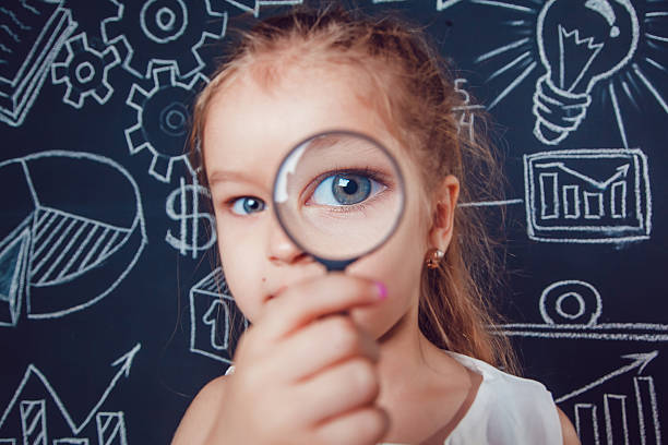istock Little girl looking through a magnifying glass on dark background 614420278