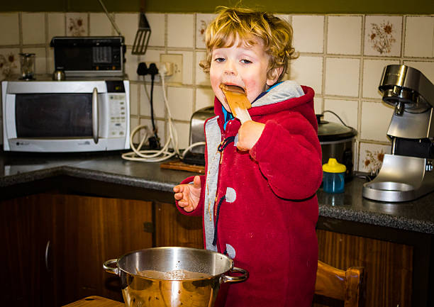 istock Little boy licking a chocolate cake batter spoon 614424542
