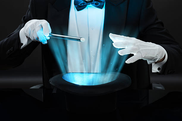 Magician Holding Magic Wand Over Illuminated Hat Midsection of magician holding magic wand over illuminated hat against black background magic trick photos stock pictures, royalty-free photos & images