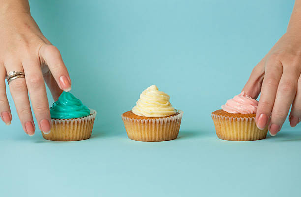 istock Closeup of female hands choosing between three colorful cupcakes 614425812