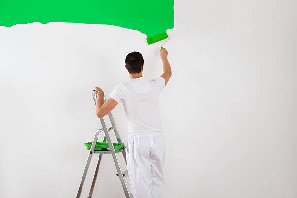 istock Man Painting Wall With Green Paint Roller 614426420