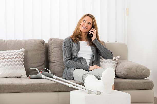 Woman With Plastered Leg Talking On Mobile Phone Mature Woman With Plastered Leg Talking On Mobile Phone At Home broken leg stock pictures, royalty-free photos & images