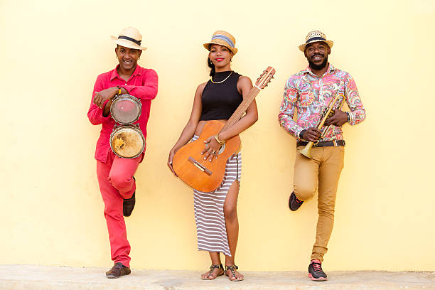 Cuban Musical Trio Cuban musical band, the trio consisting of a well known musicians standing against the bright yellow wall. Beautiful young woman standing in the middle, holding a guitar. The man on the left holding the small drums bongos, and a musician on the left holding a trumpet. Havana, Cuba rumba photos stock pictures, royalty-free photos & images