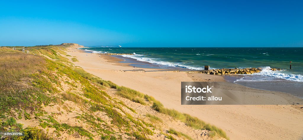 Sandy beach at Hengistbury Head Dorset England near Bournemouth Beautiful pale yellow sands on the Dorset Coast with waves breaking on the shoreline from green seas under blue skies. A fisherman sets up his rod to catch sea bass or bream. Bay of Water Stock Photo