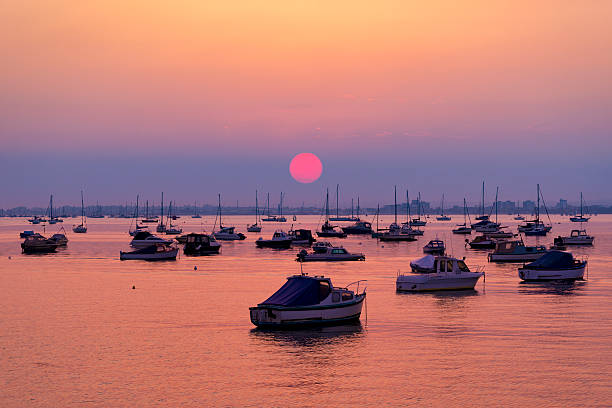 Serene sunset over boats at Sandbanks, Poole, Dorset near Bournemouth The sun sets ovr Poole Harbour. Boats are silhouetted against the bright sunlight poole harbour stock pictures, royalty-free photos & images