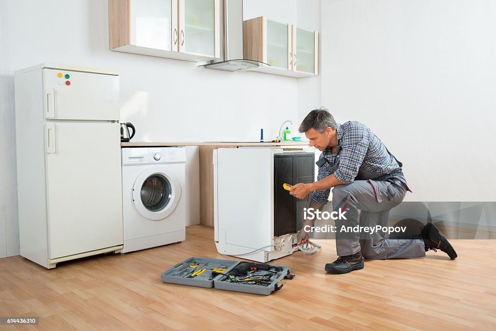 Technician Checking Dishwasher With Digital Multimeter Male technician checking dishwasher with digital multimeter in kitchen Appliance Stock Photo