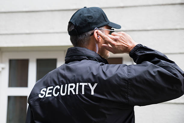 Security Guard Listening To Earpiece Against Building Rear view of mature security guard listening to earpiece against building security staff stock pictures, royalty-free photos & images