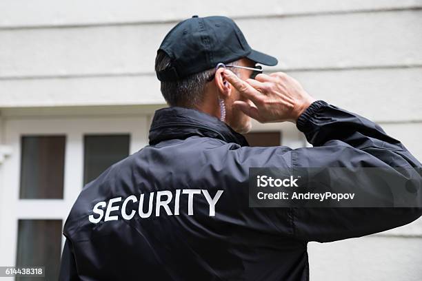 Security Guard Listening To Earpiece Against Building Stock Photo - Download Image Now