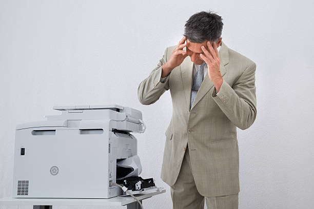 Irritated businessman looking at paper stuck in printer at office
