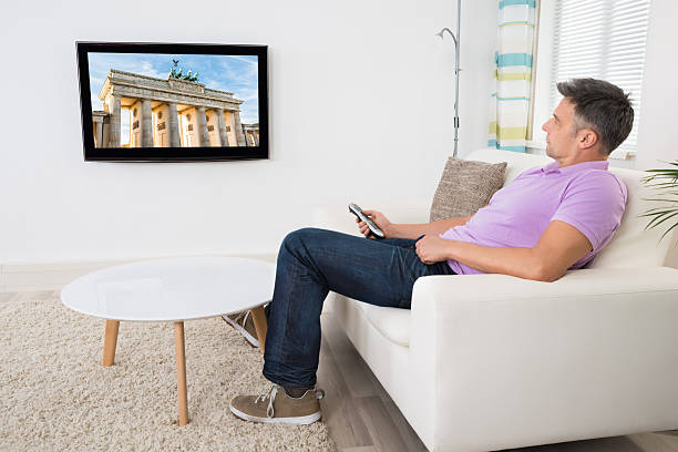 istock Mature Man Sitting On Couch Watching Television 614440624