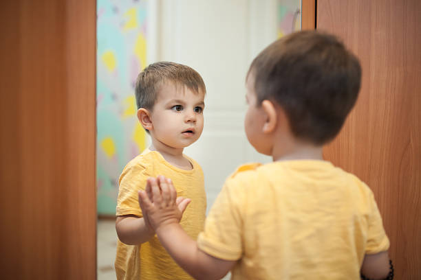 small kid staying by reflection and watching himself;