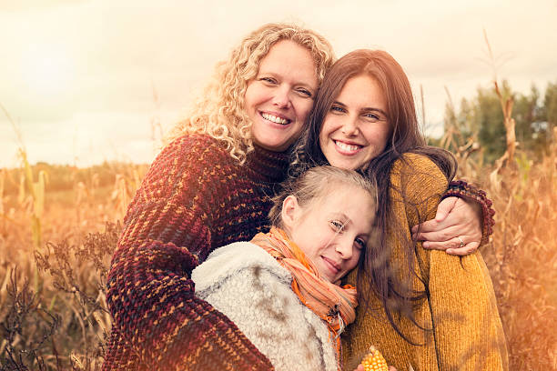 Portrait of teenagers with mother in autumn sunset outdoors. Portrait of teenagers with mother in autumn sunset outdoors. They are snuggling together, standing in a corn field. They all are wearing warm wool pullover. Waist up horizontal shot with sun flare and copy space. This was taken in Quebec, Canada. single mother photos stock pictures, royalty-free photos & images