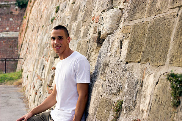 istock Young man in a white shirt leaning on a wall 614442388