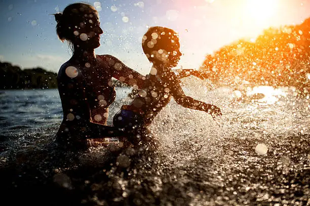 Photo of mother swim with baby in blue water at sunset;