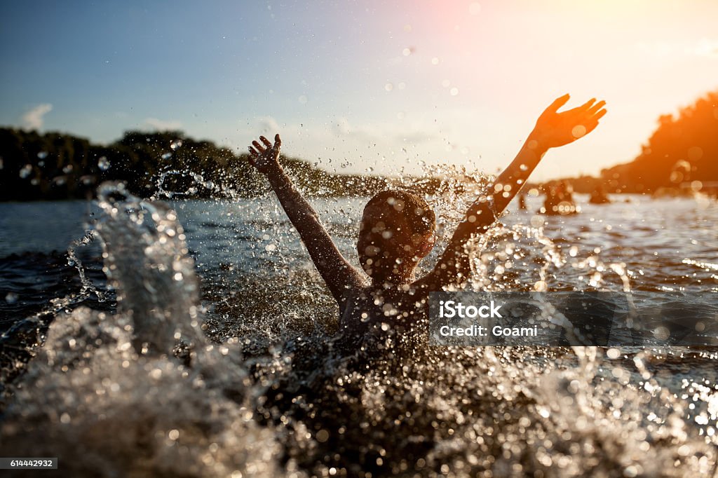 little kid play in water and making splash; child swim in lake or river and have fun with drops; Lake Stock Photo