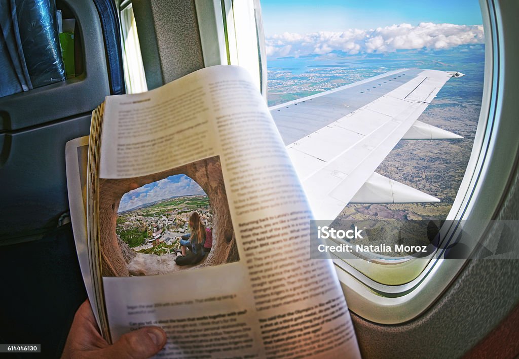 Woman is sitting   by window on a plane with magazine Woman is sitting   by window on a plane with magazine in hands. Concept art. Travel Stock Photo