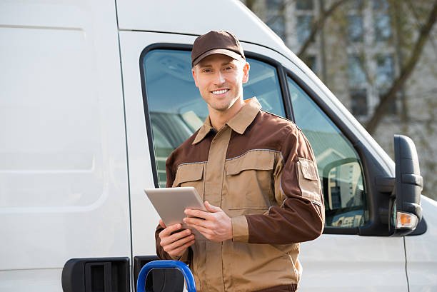 istock Smiling Delivery Man Holding Digital Tablet Against Truck 614446558